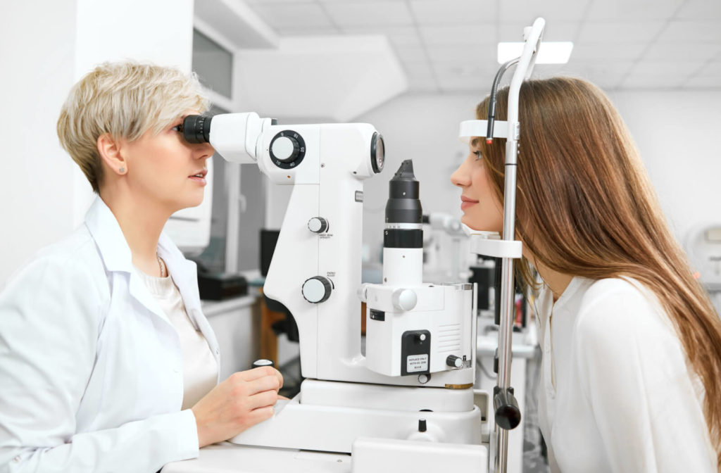 A female optometrist examining the eyes of a young woman using a medical device to detect potential eye problems