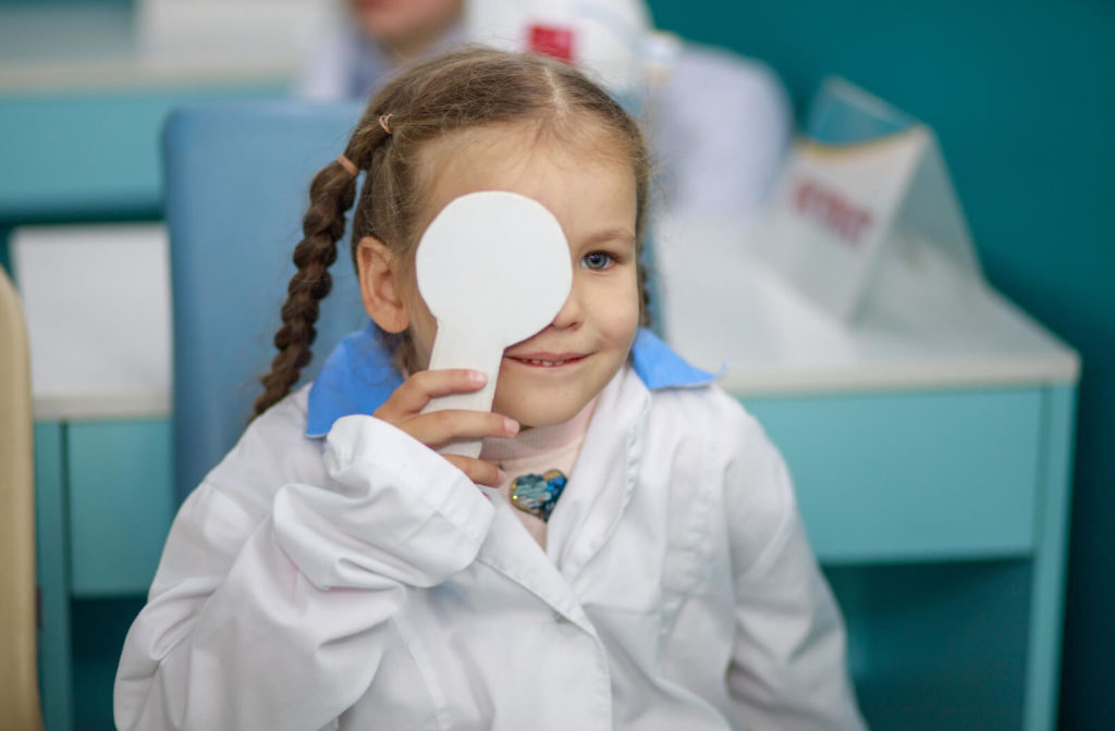 A young girl undergoing an eye examination while holding a white occluder.