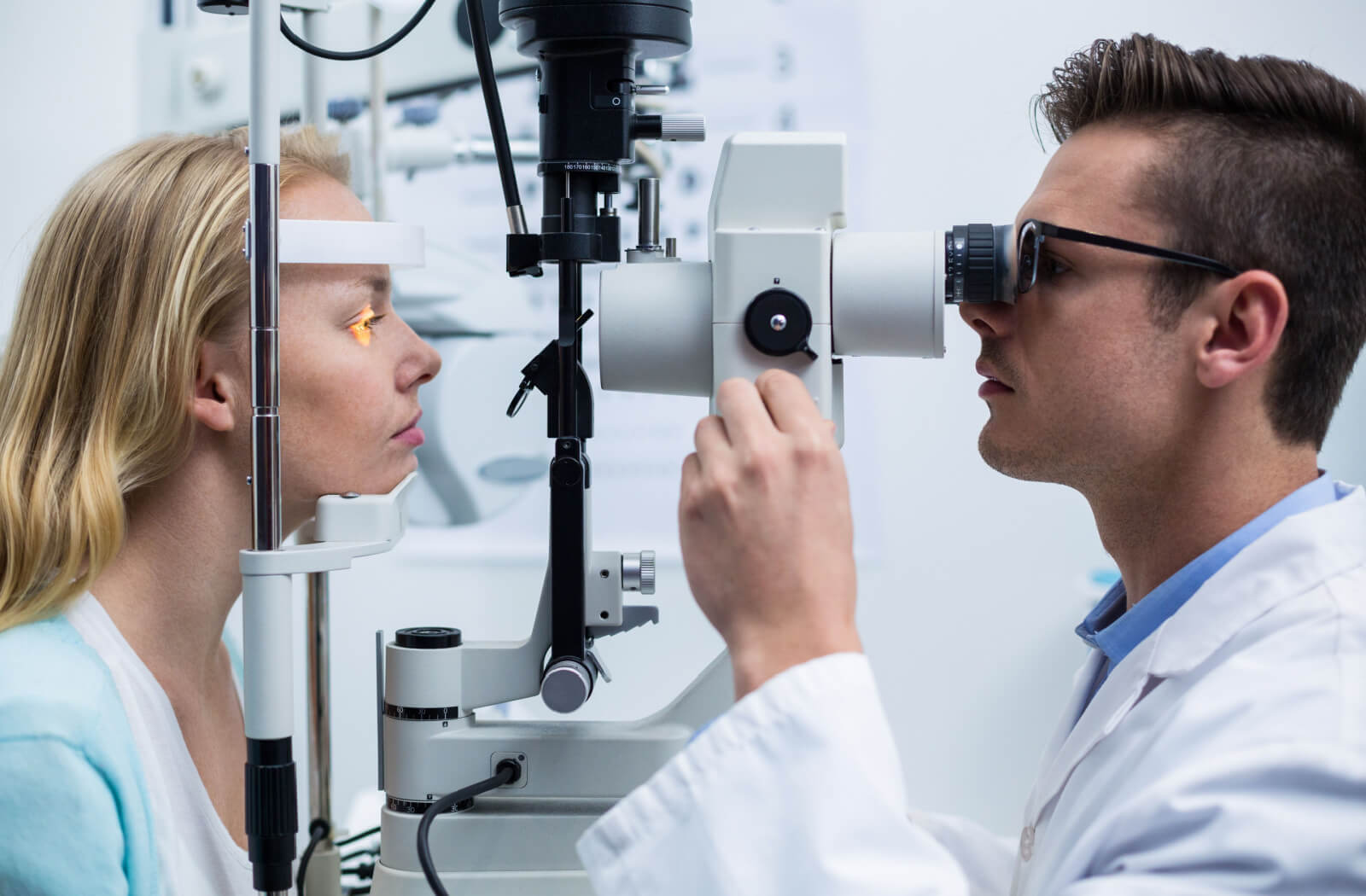 A woman looking into a piece of optometry equipment as her male optometrist performs an eye exam